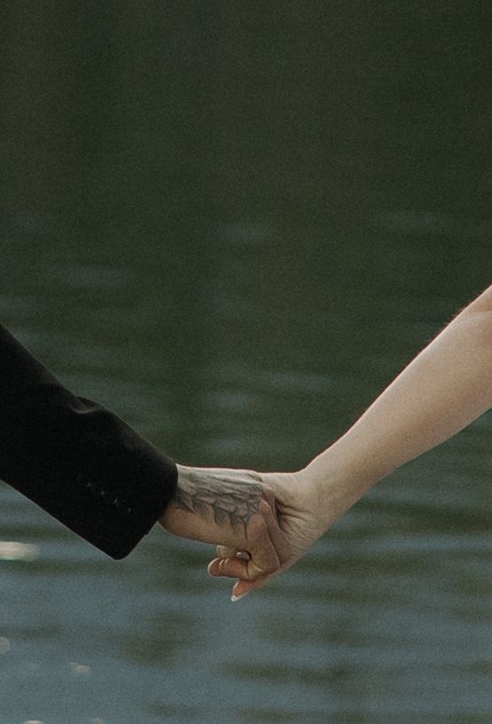 Two hands reaching out to hold each other tenderly against a dark green blurred background.