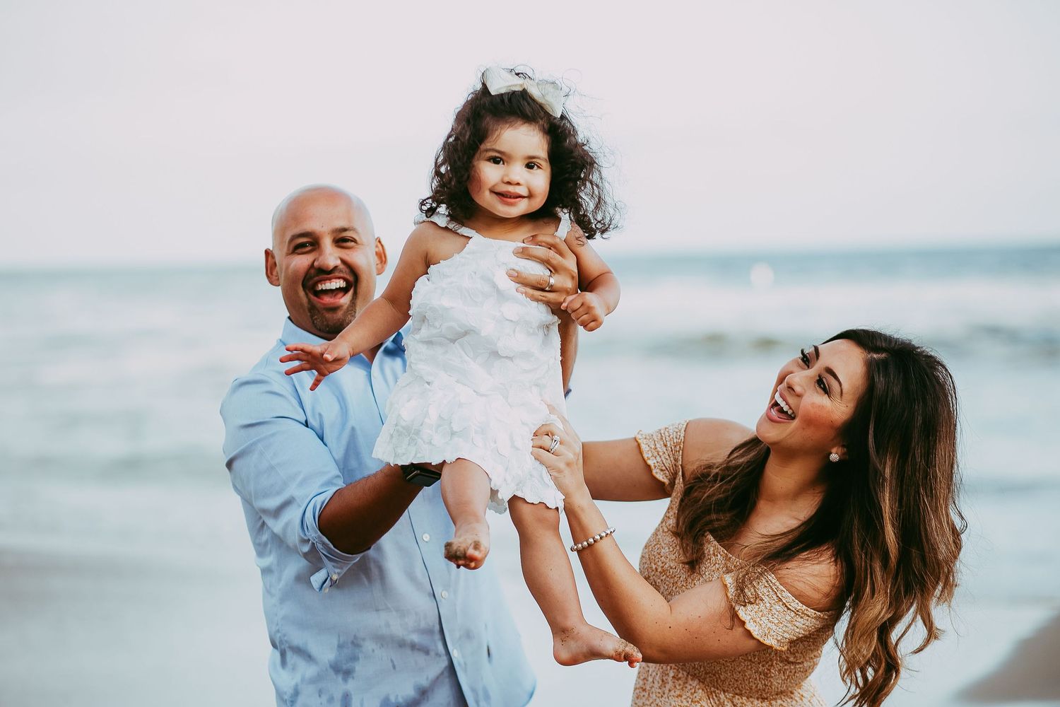 A joyful family plays together and embraces on a sunny beach with waves and sand in the background.