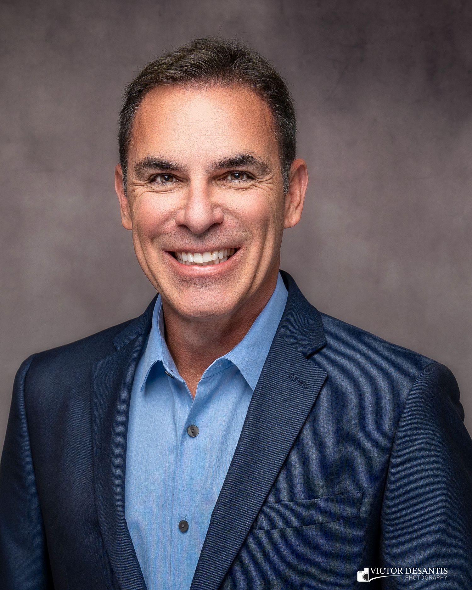 Professional headshot series showing a person in a navy suit and light blue shirt with varied expressions.