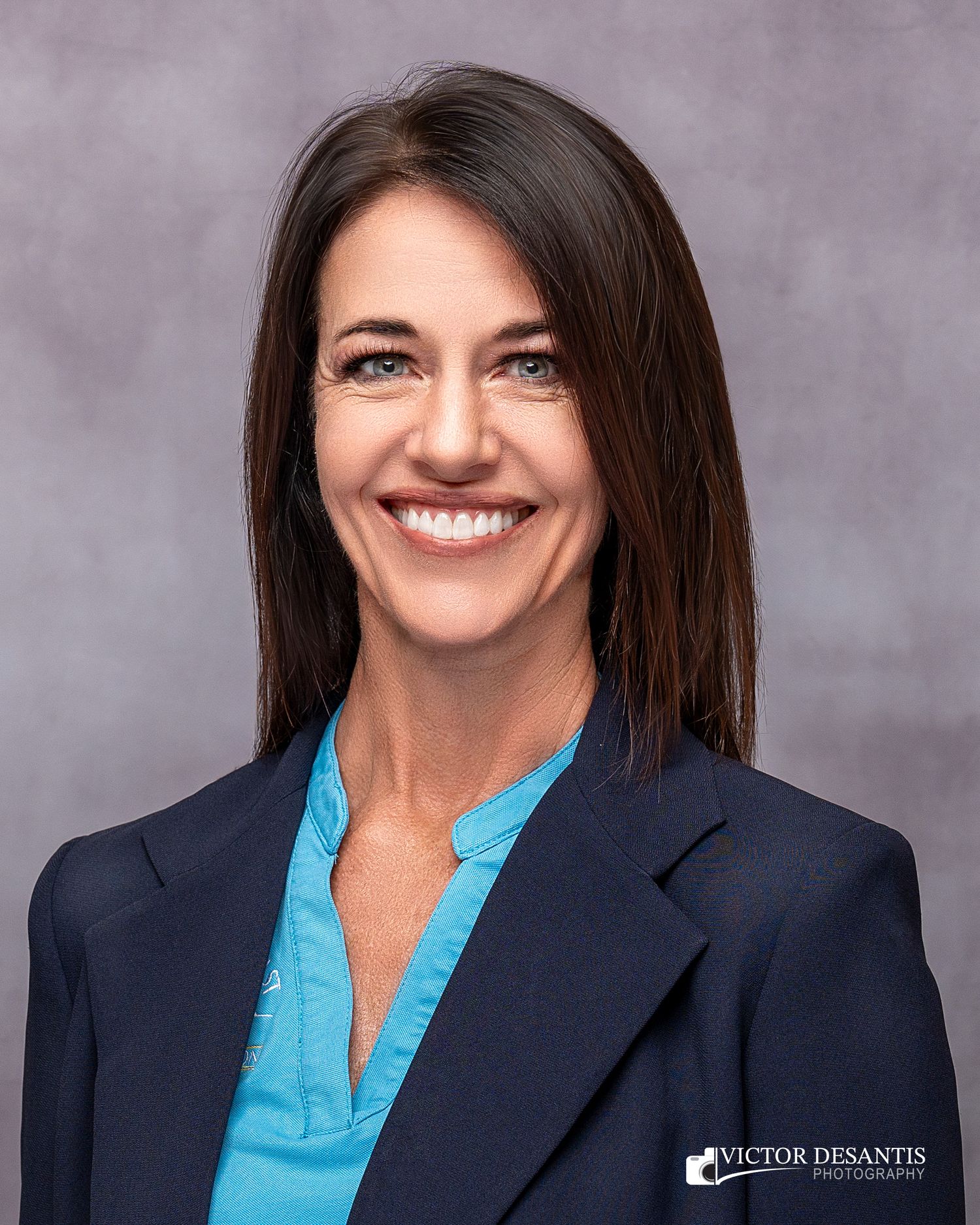 Professional headshot in navy blazer and bright blue blouse against a muted purple backdrop.