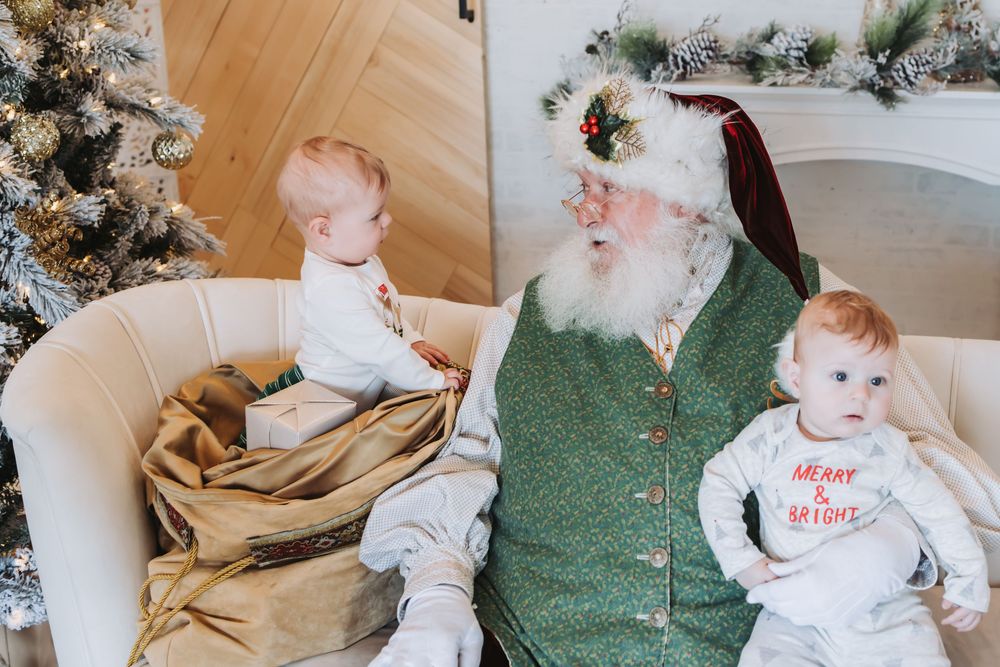 Baby in white onesie crawls and plays on green carpet with festive Christmas decorations in background.