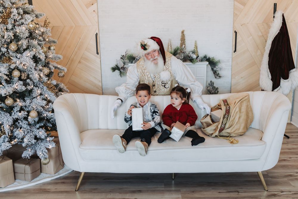 Festive holiday scene with children playing on a white couch next to a flocked Christmas tree decorated in gold ornaments.