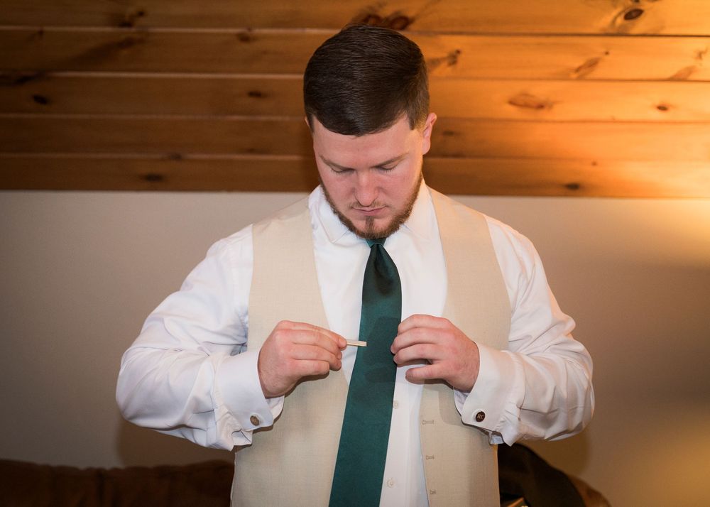 Groomsman adjusting green tie in formal wedding attire.