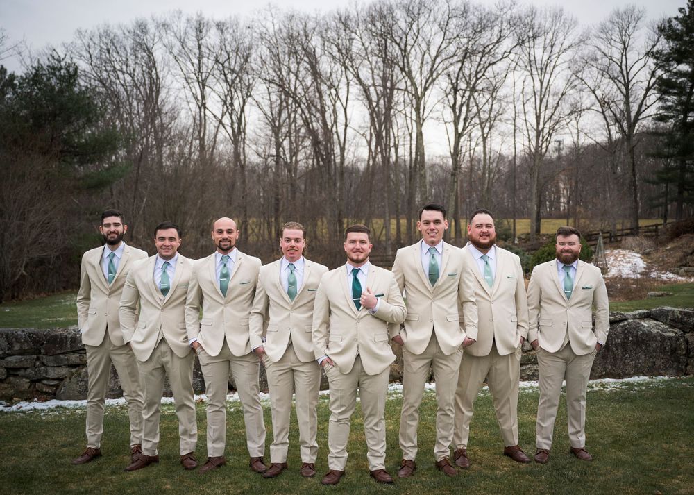 Wedding party in cream colored suits lined up outdoors for formal group photo.