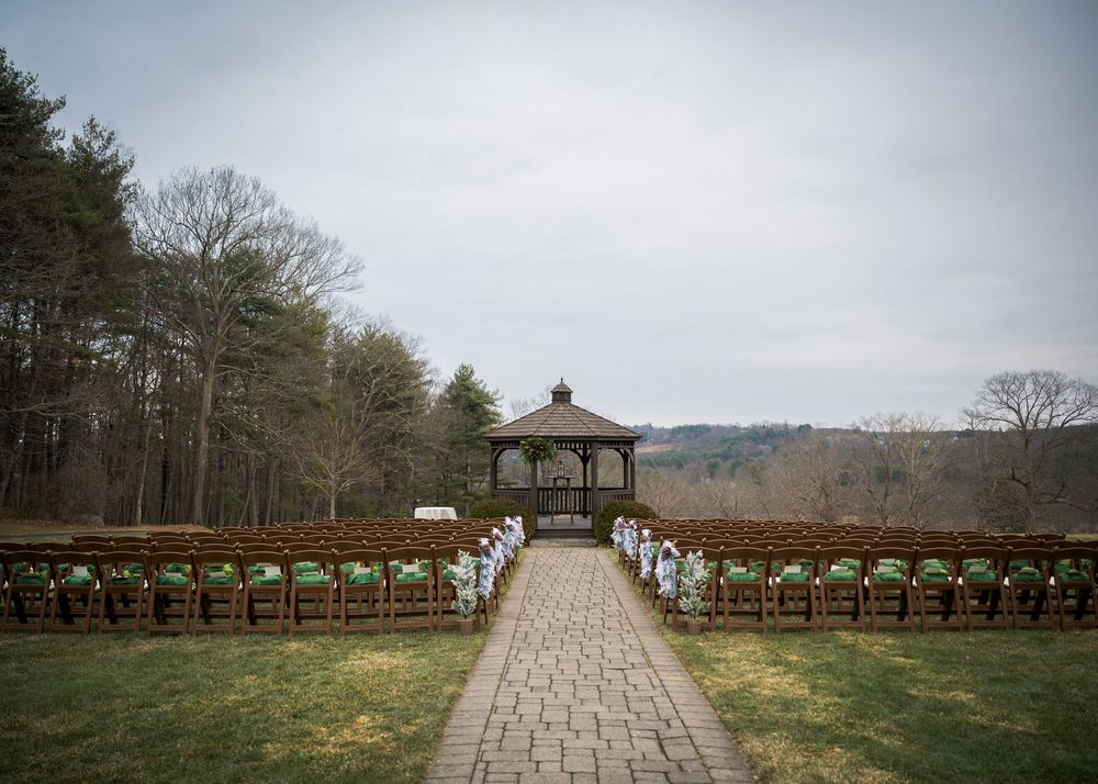 Stone pathway leads to a wooden gazebo set against a cloudy sky at wedding venue.