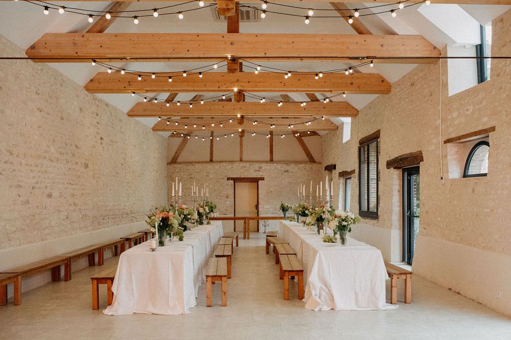 Elegant barn wedding reception with fairy lights, wooden beams, long tables and floral centerpieces.