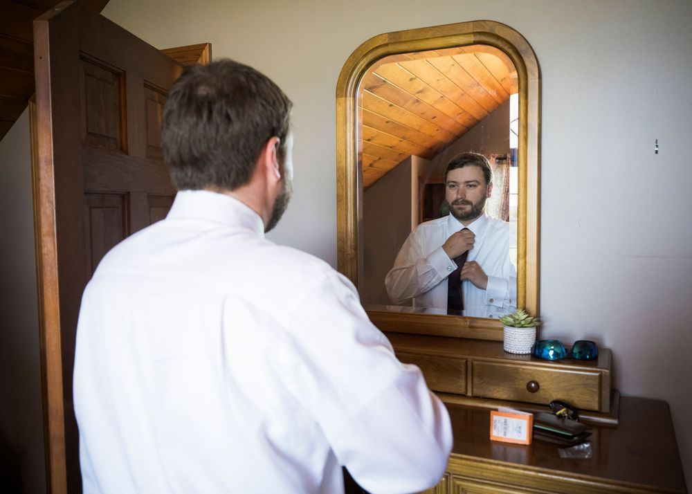 A person in white shirt looks in a bathroom mirror while standing near a wooden door frame.