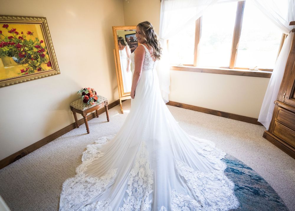 A flowing white wedding dress with intricate lace details laid out on a beige carpet.