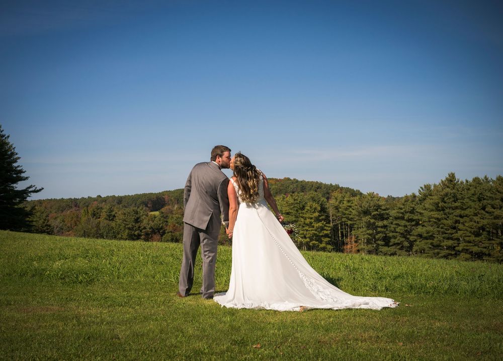 Wedding couple poses in an open field against a blue sky and rolling hills landscape.