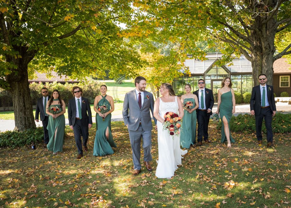 Wedding party members stand under autumn trees in a scenic outdoor setting during a fall celebration.