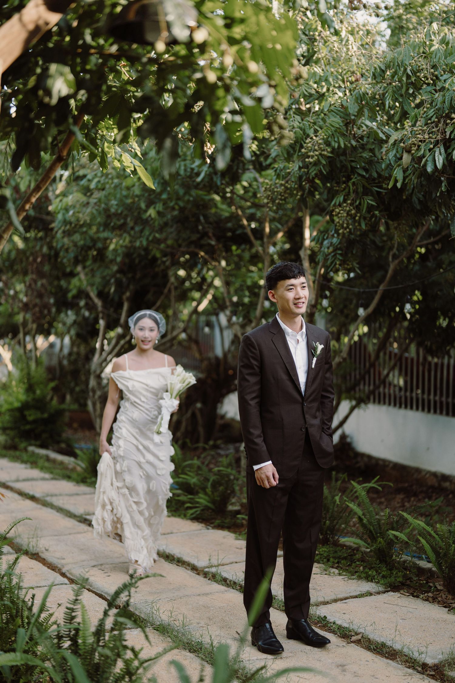 A couple poses along a garden pathway with lush greenery and trees.