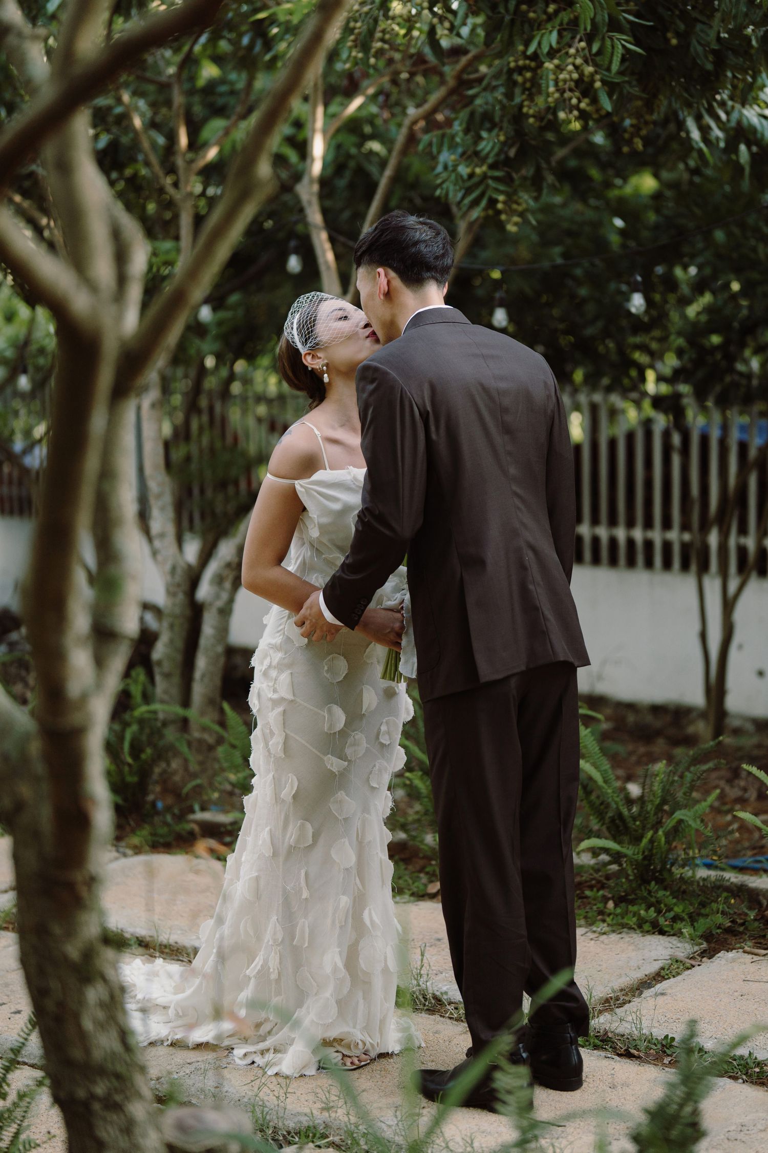 A romantic garden scene with elegant formal attire among trees and foliage.