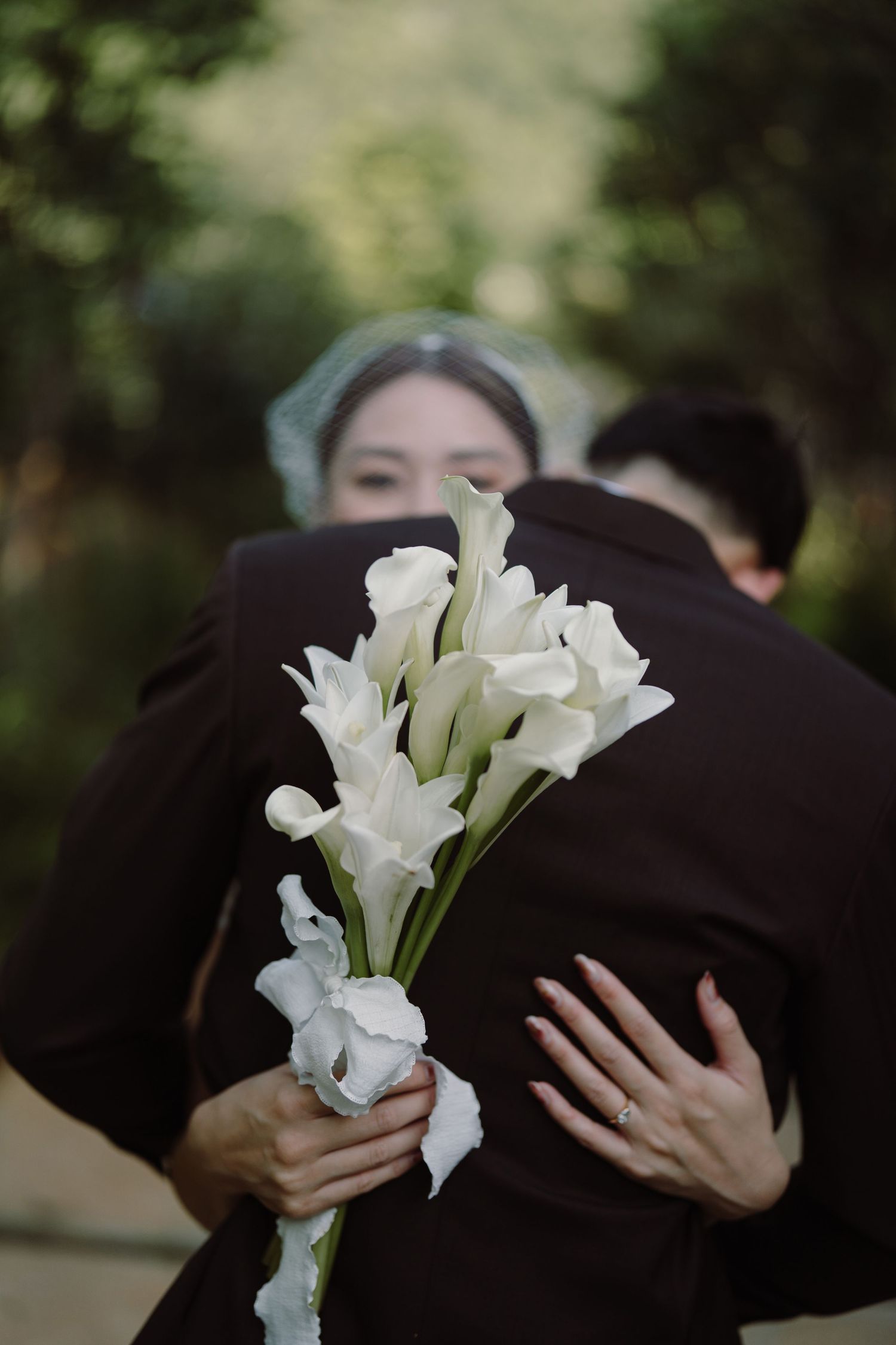 White calla lilies are held against dark formal attire in an intimate wedding photograph.