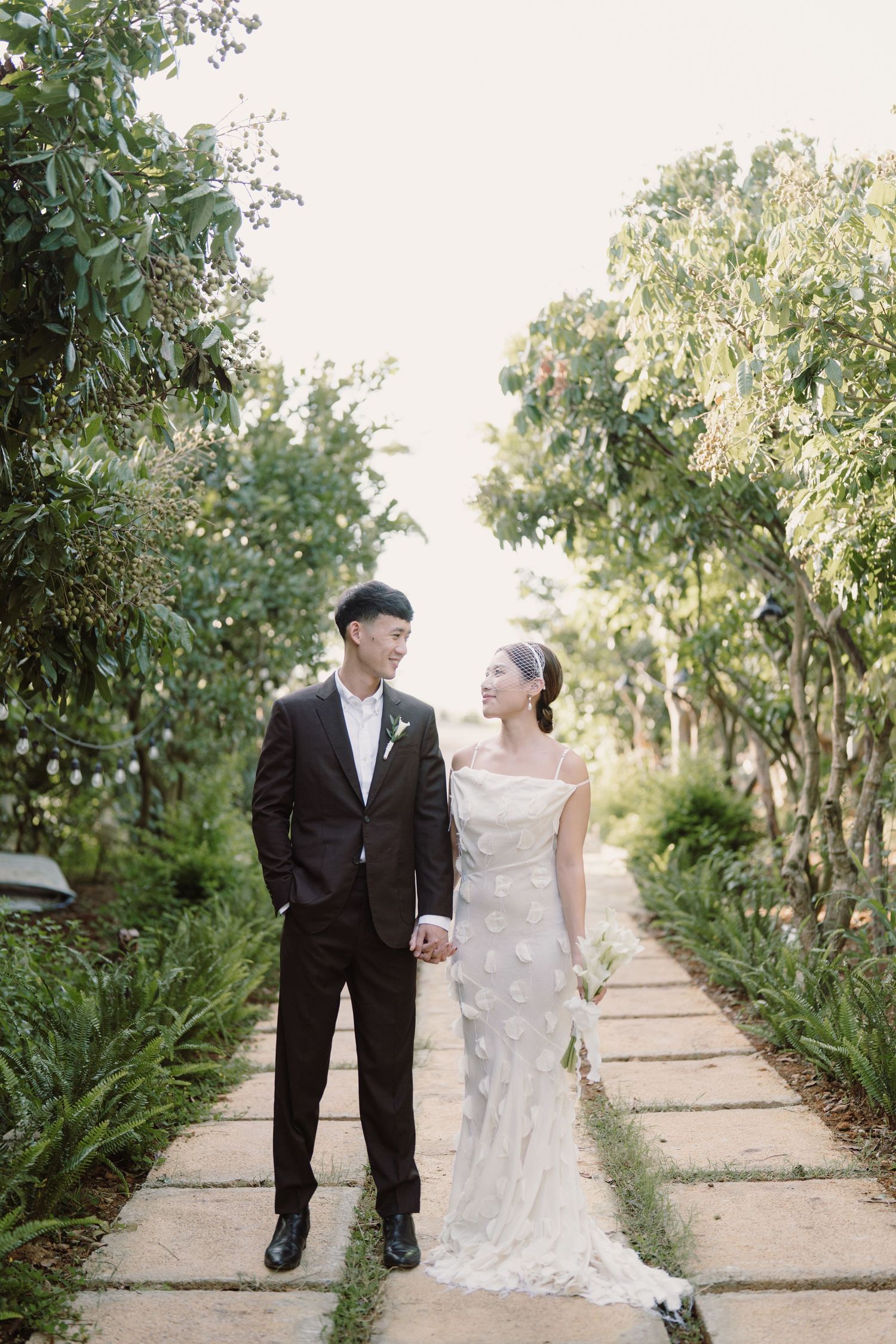 A couple walks along a tree-lined path during a wedding photoshoot.