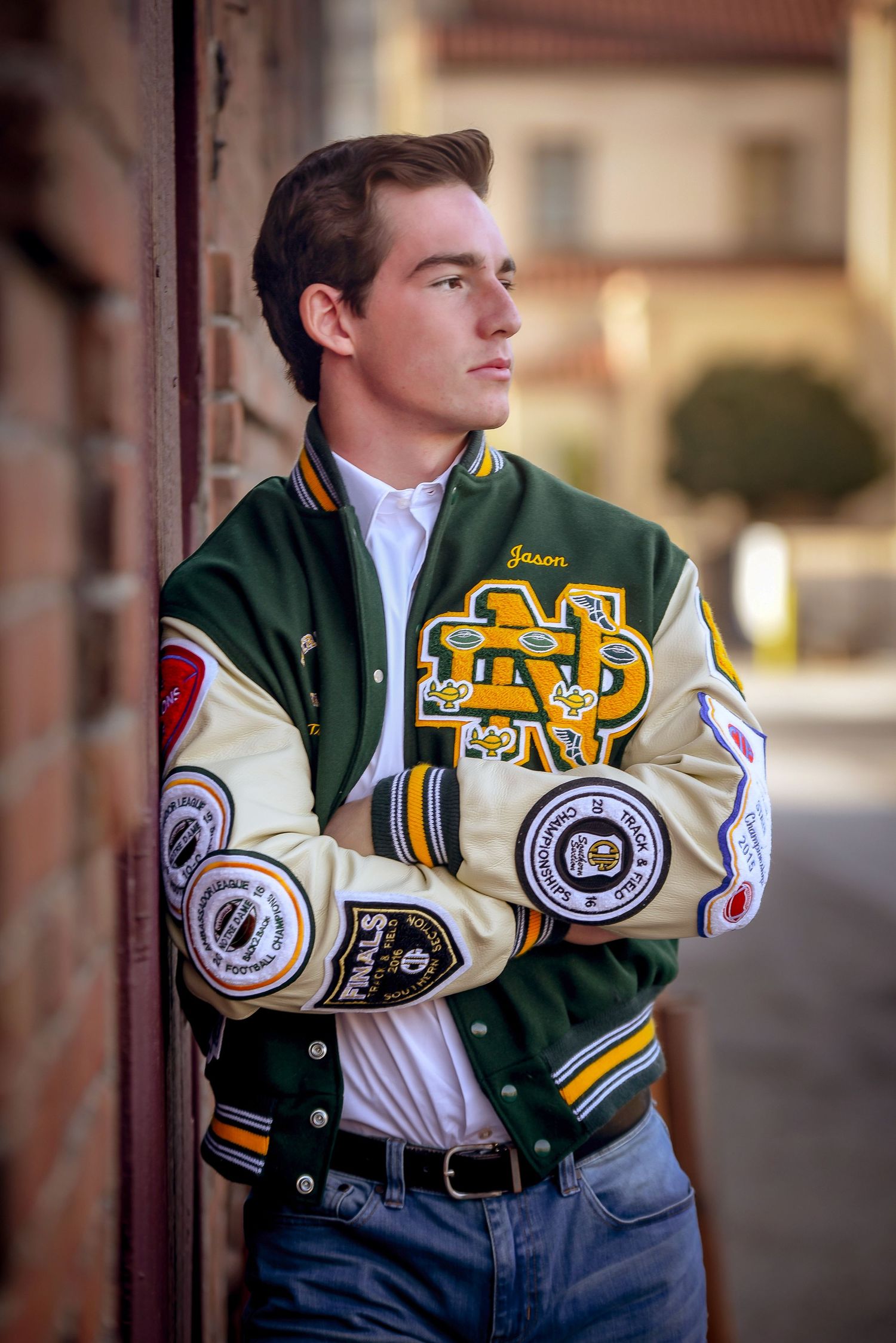 Student athlete poses in varsity letterman jacket showing school pride and sports patches.