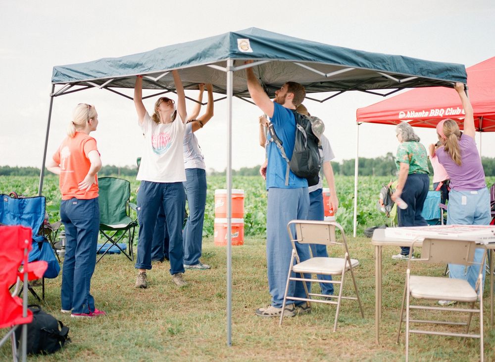 Outdoor event tents and canopies set up in grassy field with vendors and attendees under shade structures.