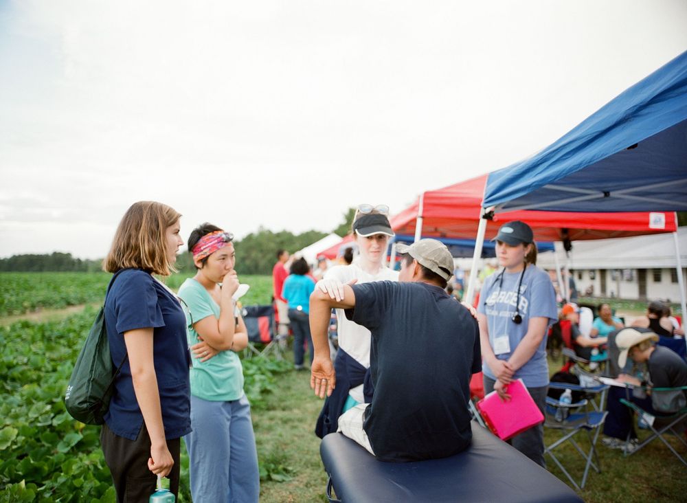 A row of outdoor massage tables set up under tents at a community event with people providing treatments.