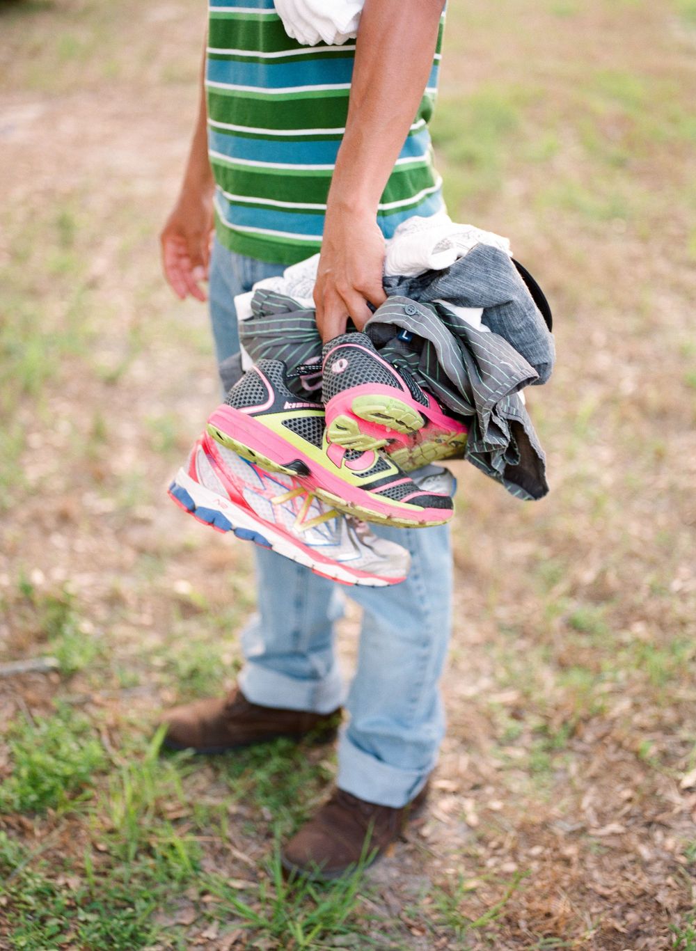 Person holding a pile of sneakers with colorful pink and gray athletic shoes outdoors on grassy ground.
