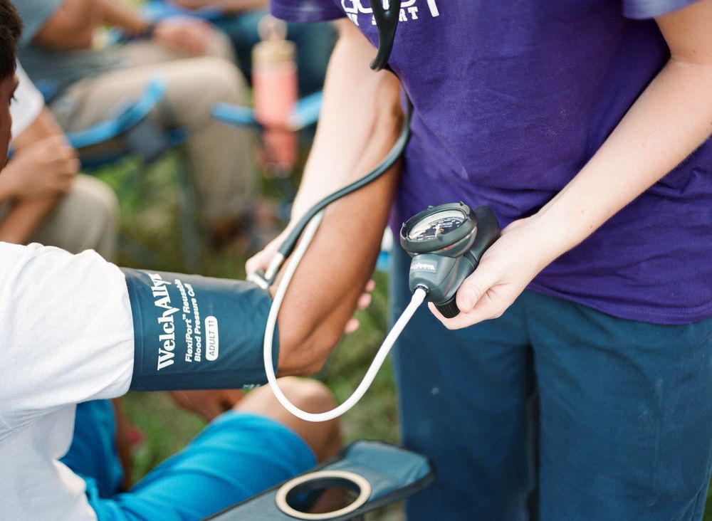 Medical professional taking blood pressure reading with manual sphygmomanometer cuff and stethoscope on patient's arm.