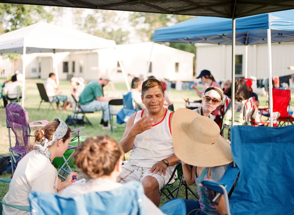 People gathered outdoors at a community event with tents and chairs on a sunny day.