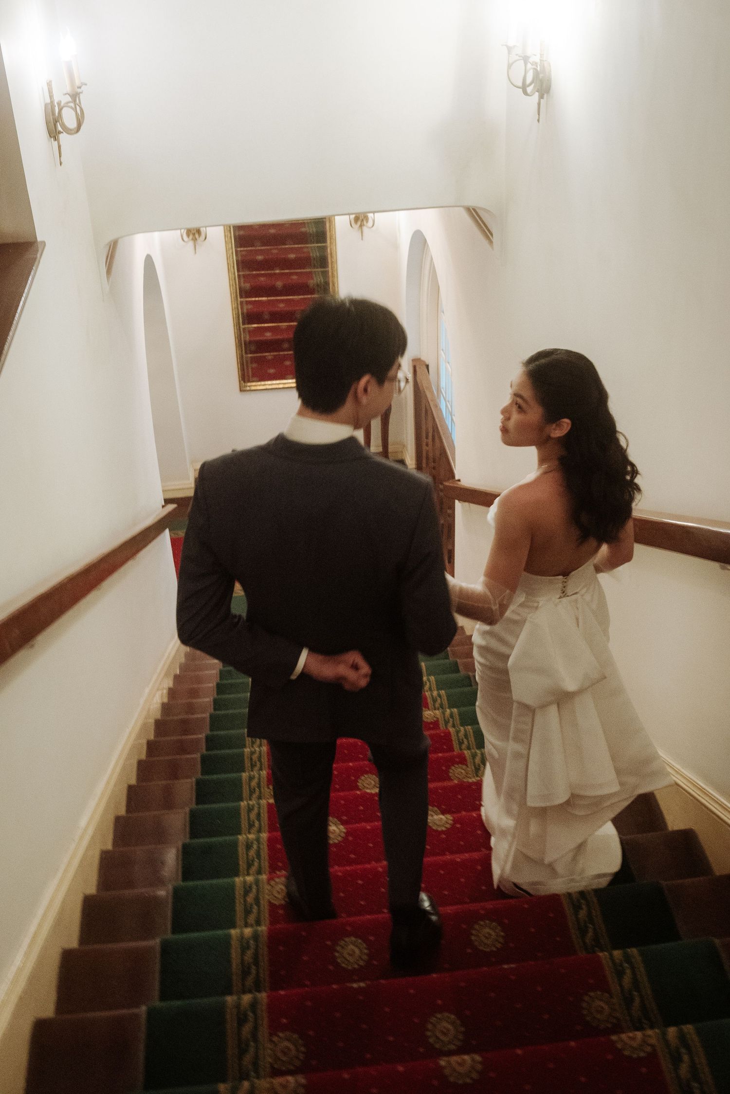 Bride and groom walk up a grand staircase with red carpet in a classic wedding venue.