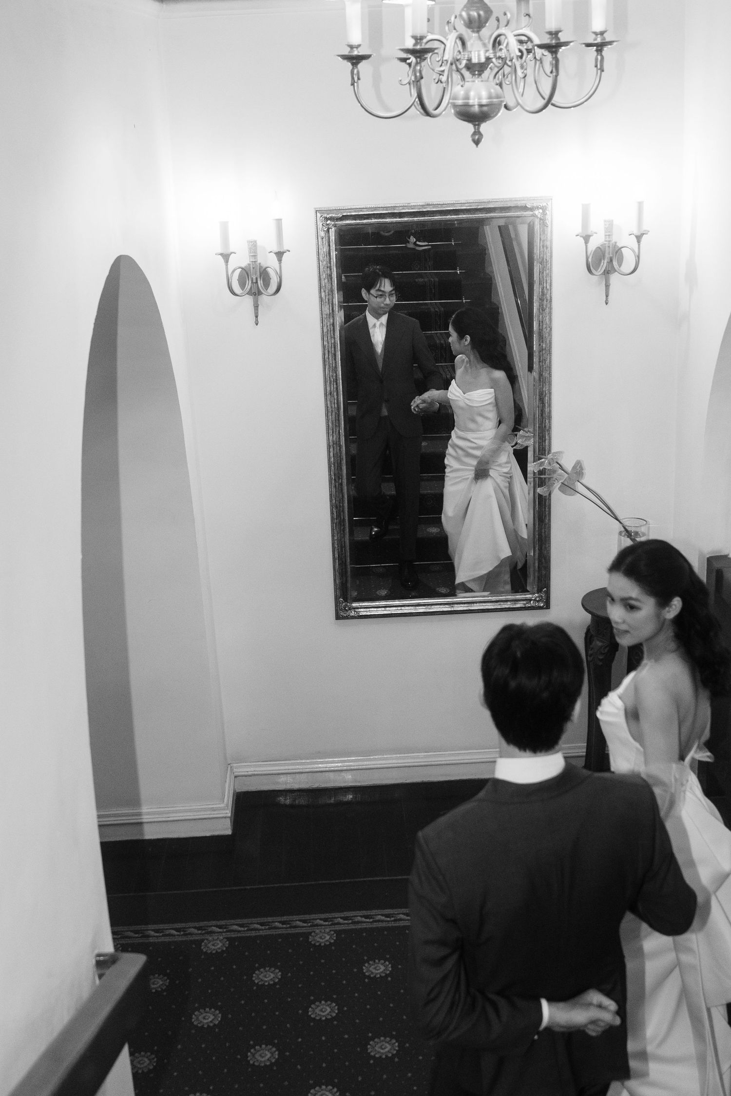 Bride and groom share a romantic moment reflected in an ornate mirror in an elegant hallway.