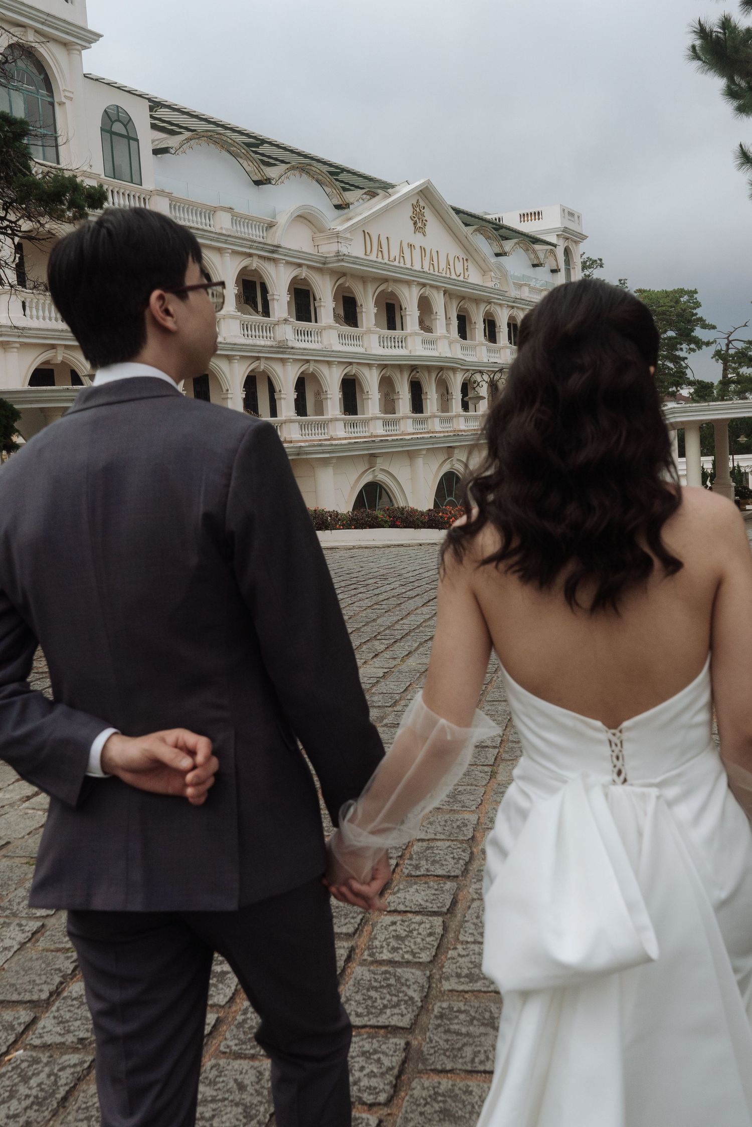 Couple holds hands walking toward the historic Dalat Palace hotel on their wedding day.