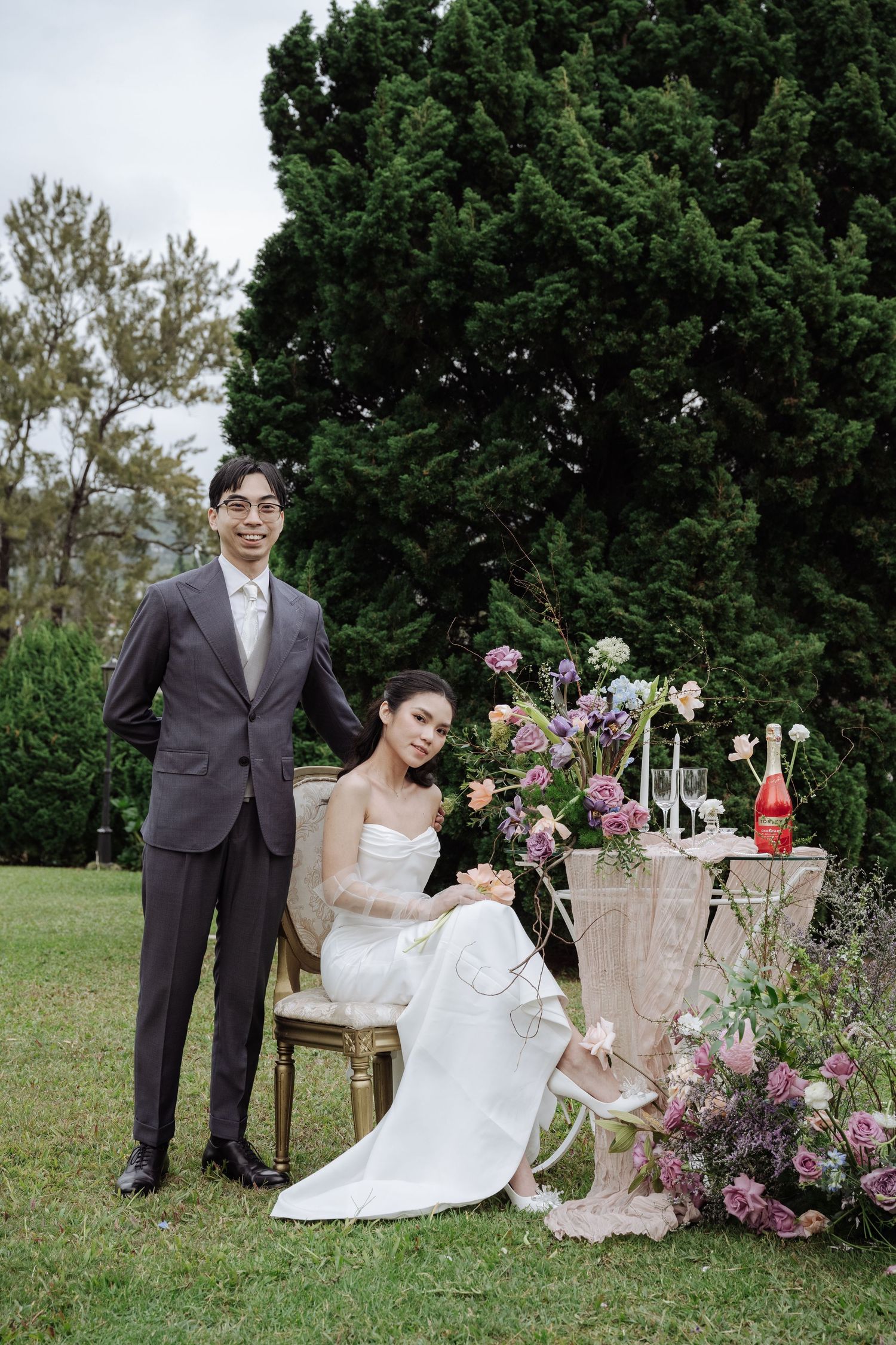Bride and groom pose beside a romantic floral tablescape in a lush garden wedding setting.