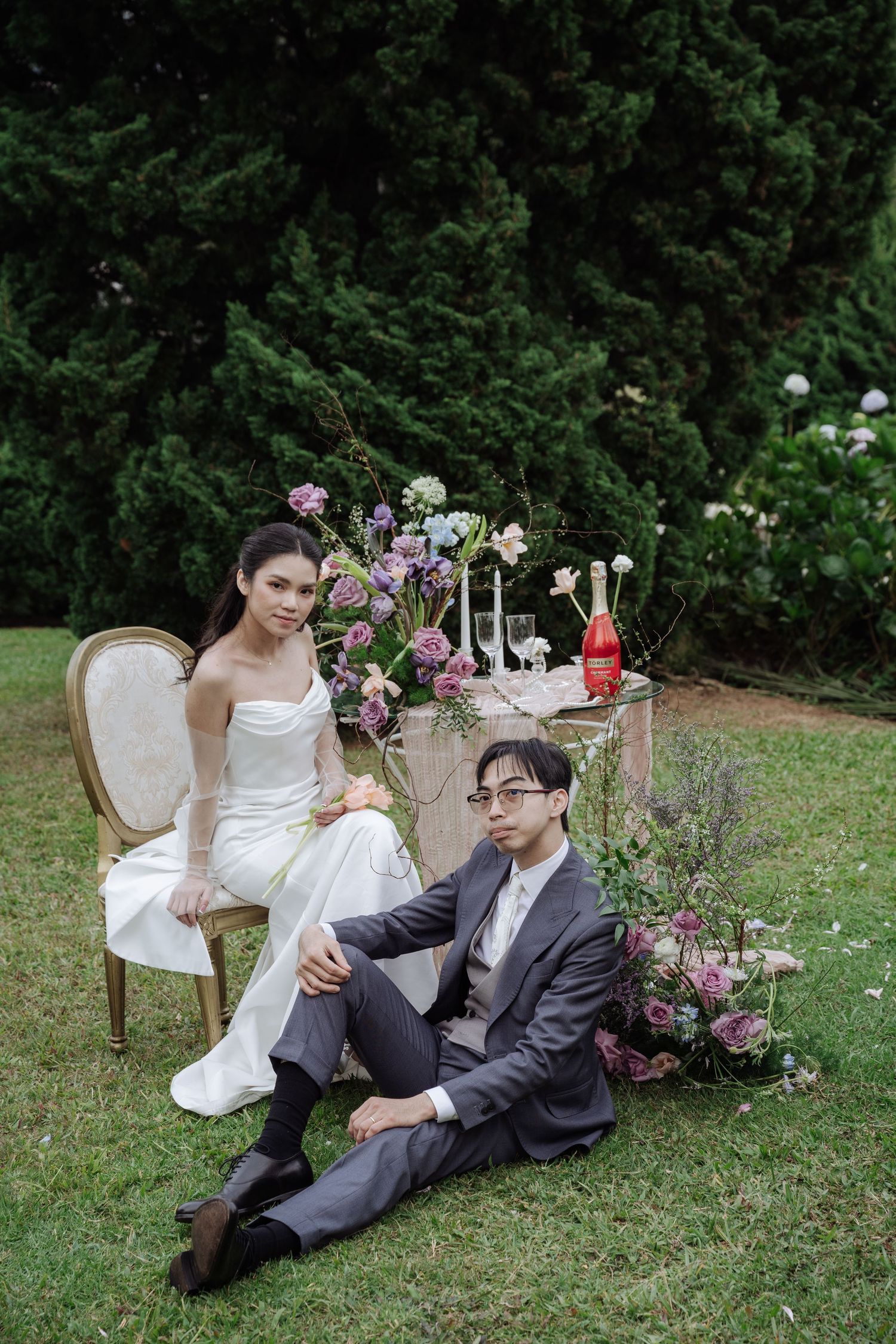 Elegant wedding couple posing in garden with floral table decor and champagne bottle.