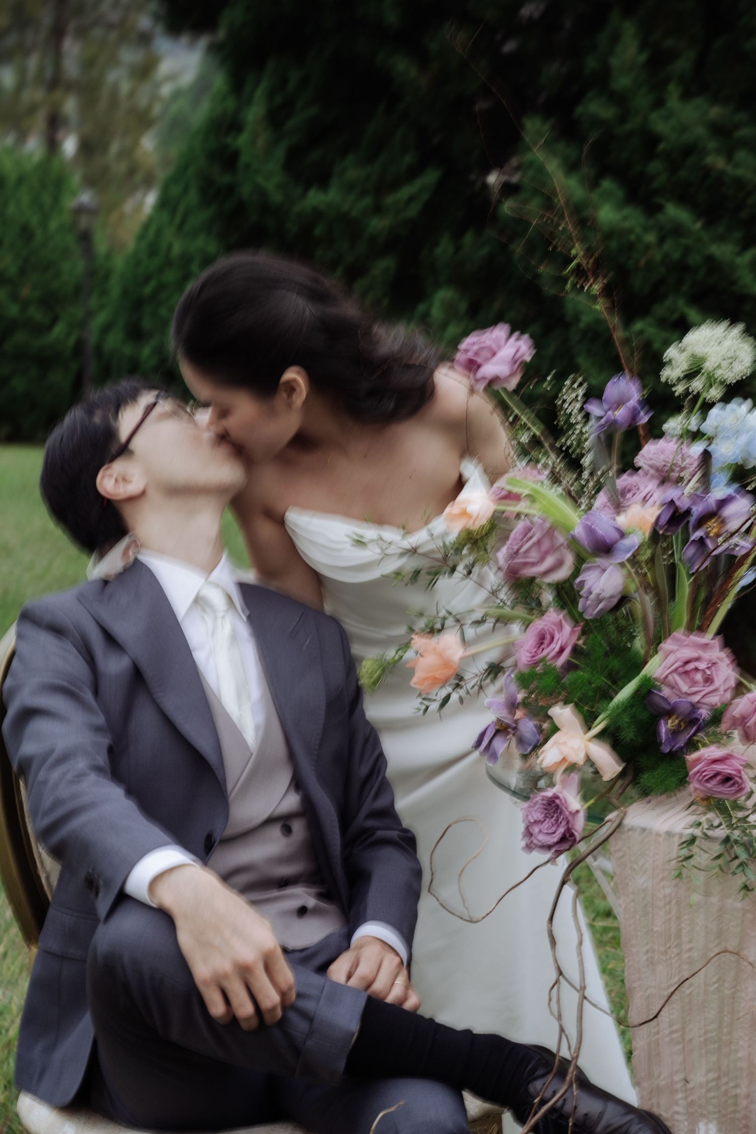 Bride and groom sharing a romantic kiss beside colorful purple and pink floral arrangement.
