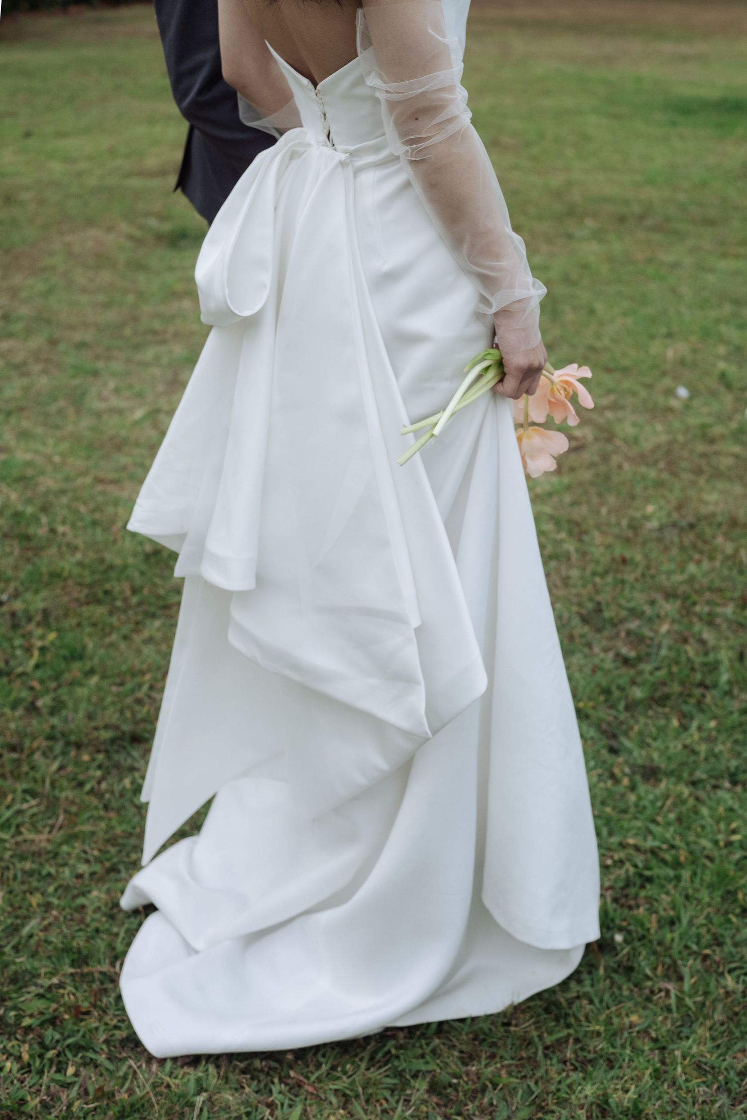 Close-up of bride in white wedding gown with large bow holding a single peach tulip.