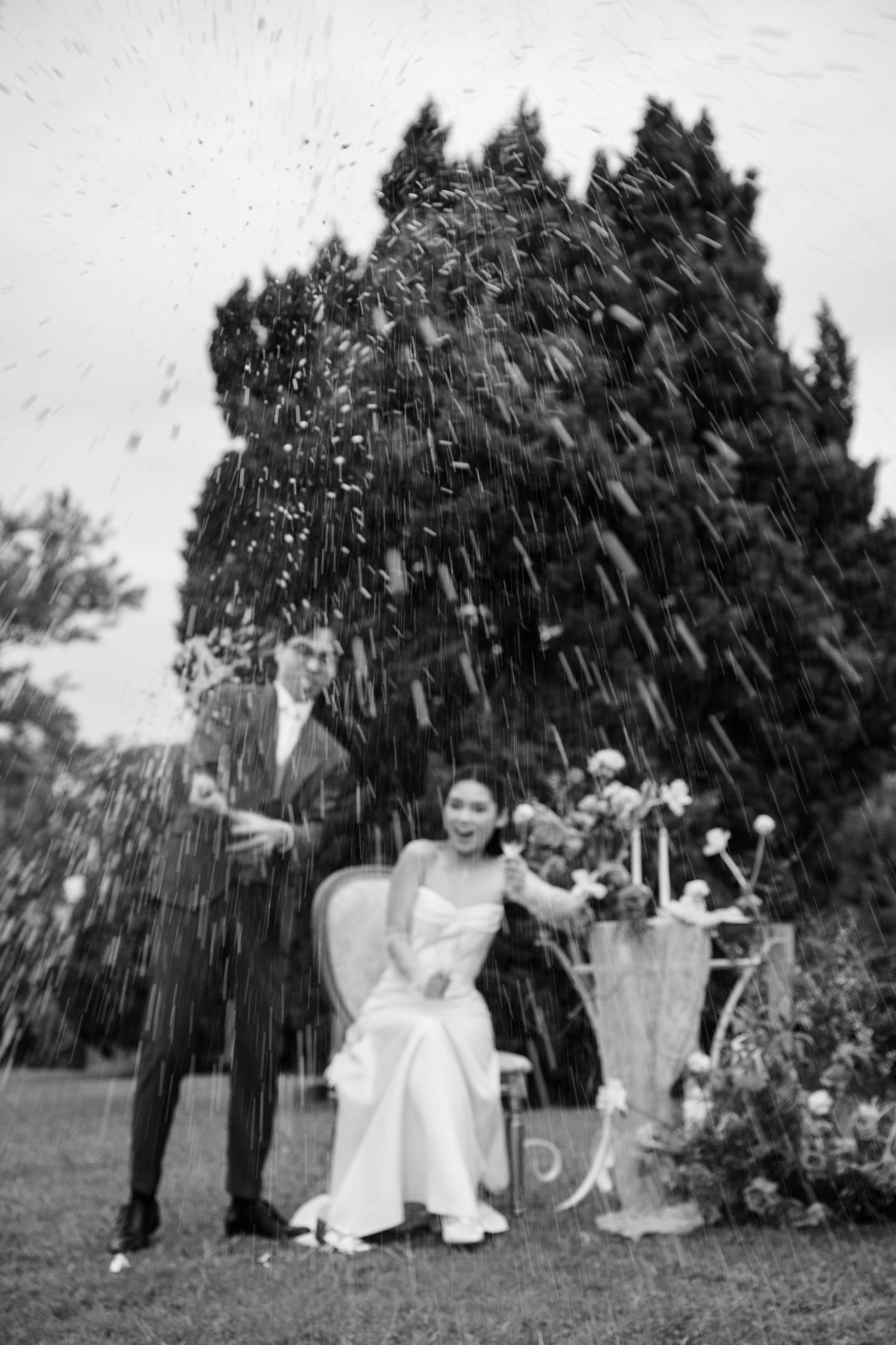 Black and white photo of couple celebrating with champagne spray at outdoor garden wedding.