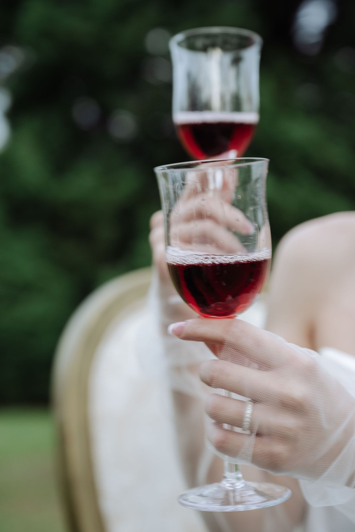 Close-up of two hands holding elegant wine glasses filled with red wine at wedding.