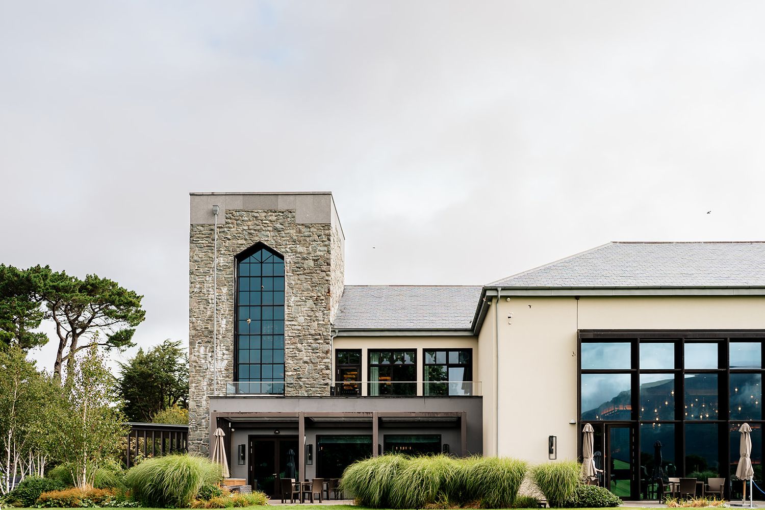 Modern single-story building with a stone tower and glass facade set against a rural landscape.