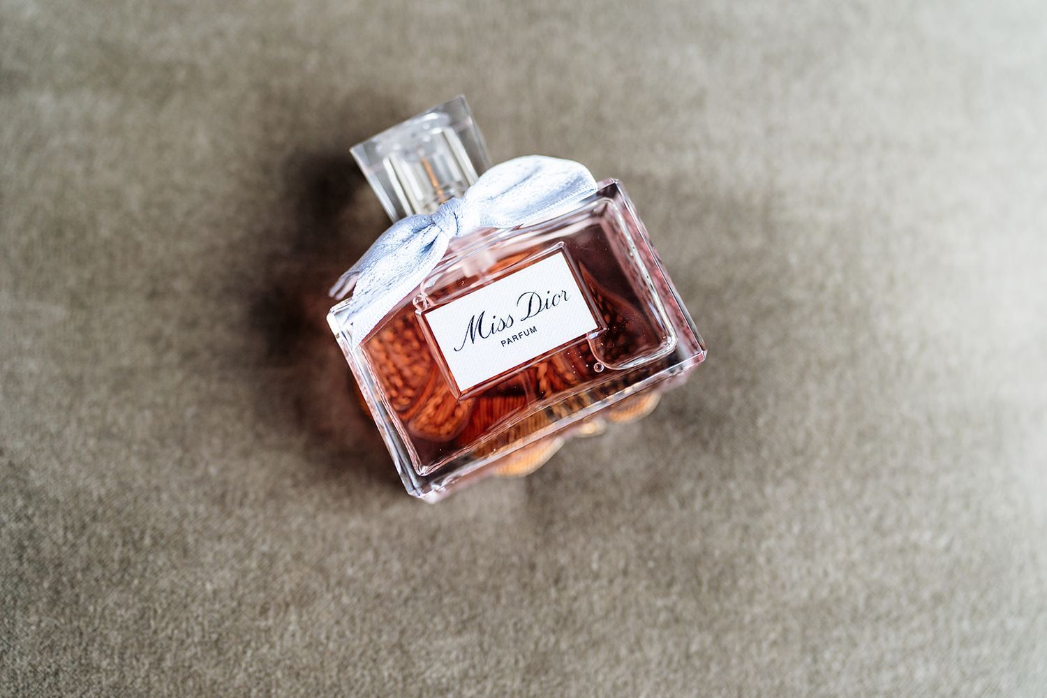 Luxury perfume bottle photographed in different angles on a textured gray fabric surface showing its elegant design.