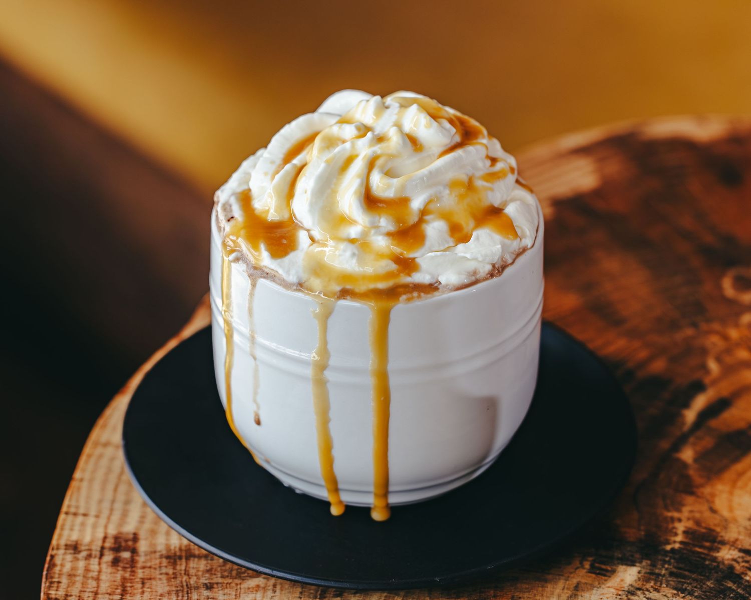 A decadent whipped cream dessert drizzled with golden caramel sauce in dramatic lighting.