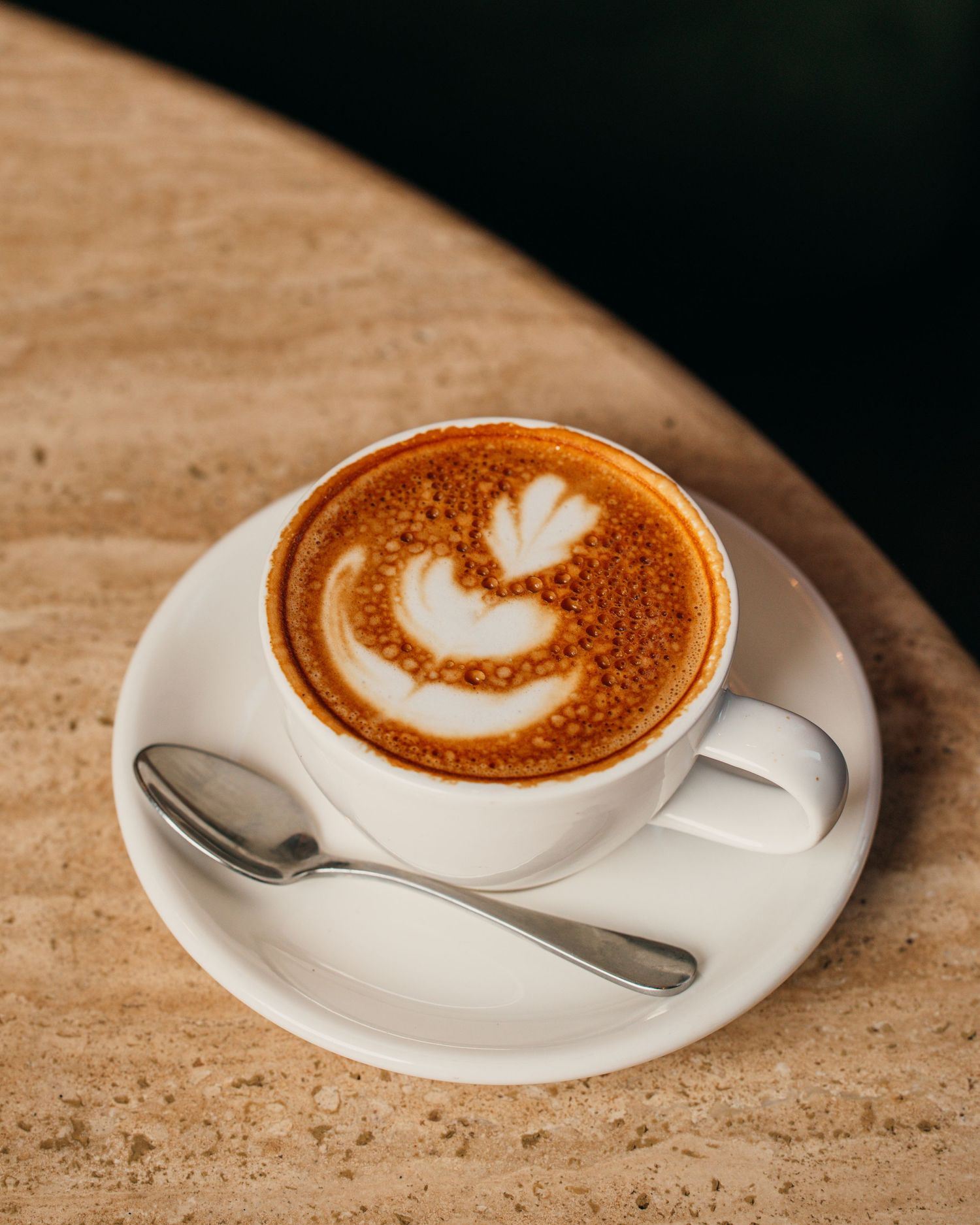 Four artisanal latte cups with heart-shaped foam art designs on a textured stone surface.