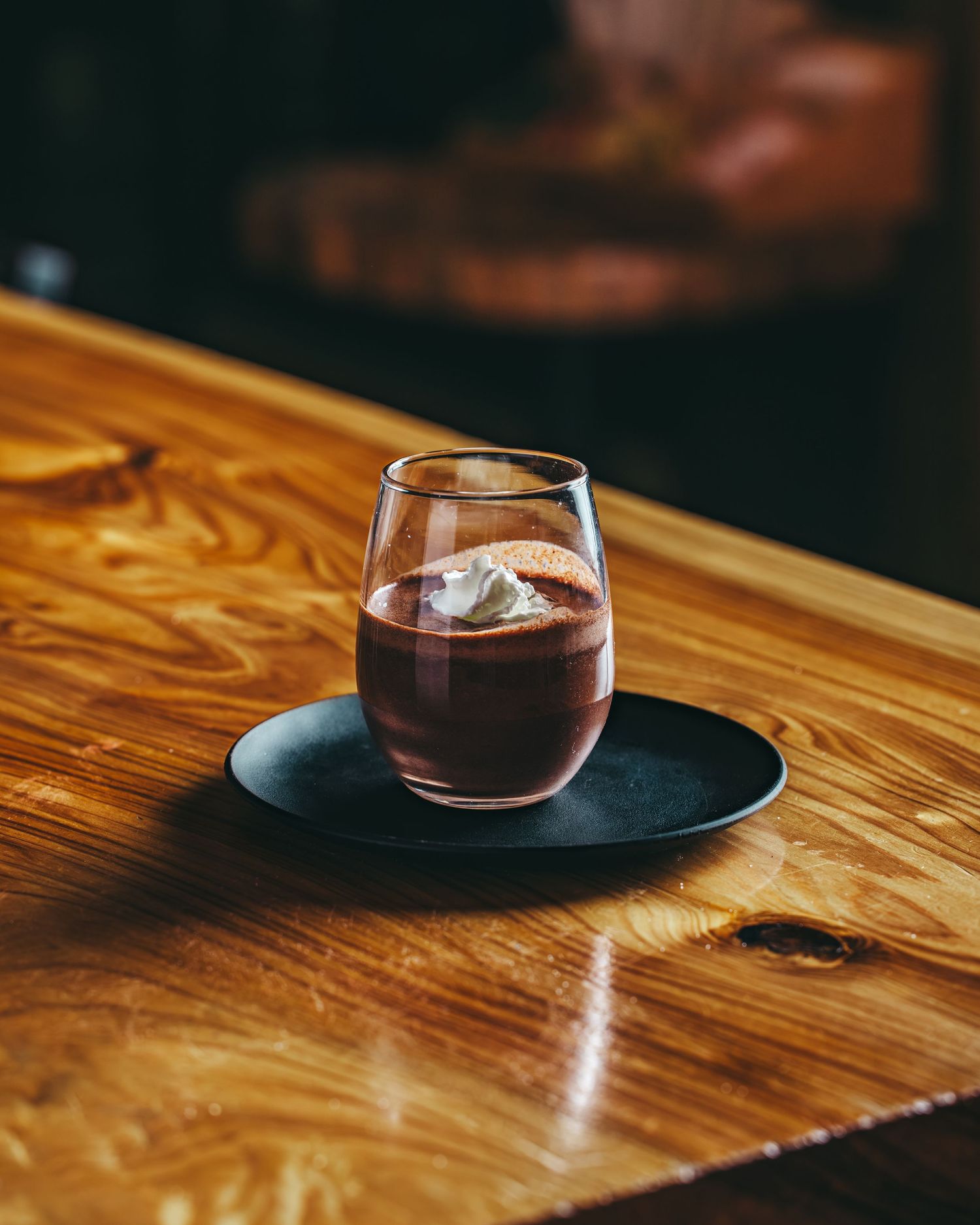 Glass of red wine or cocktail served on a black plate atop wooden table surface.