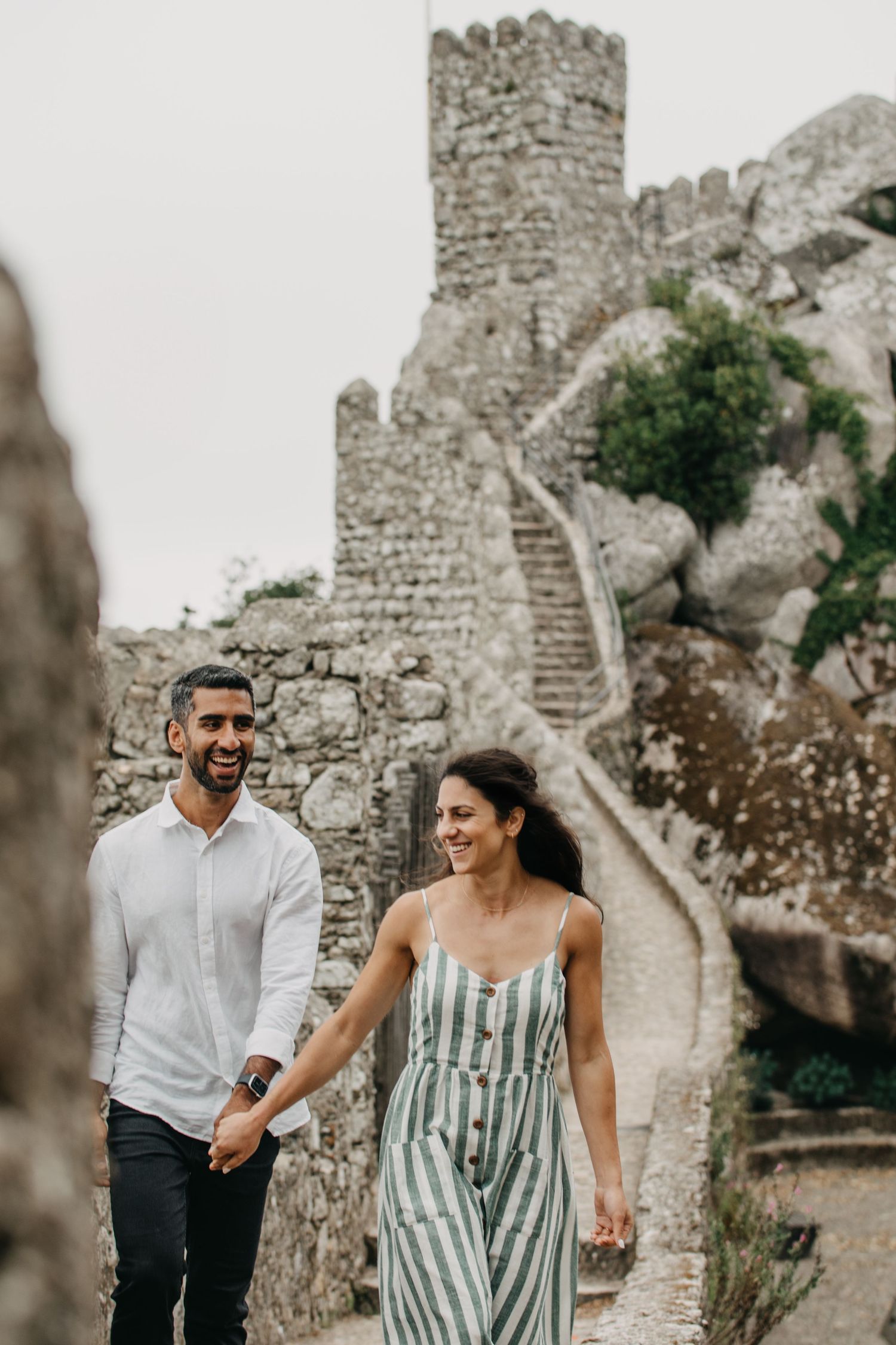 Happy couple holding hands and walking near ancient stone castle ruins on a cloudy day.