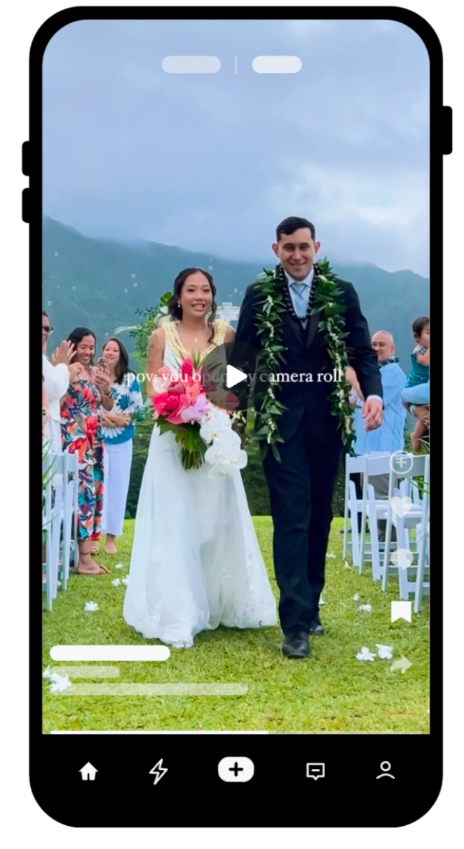 Newlyweds wearing traditional wedding attire with green leis walk together on grassy lawn with mountain backdrop at outdoor ceremony.