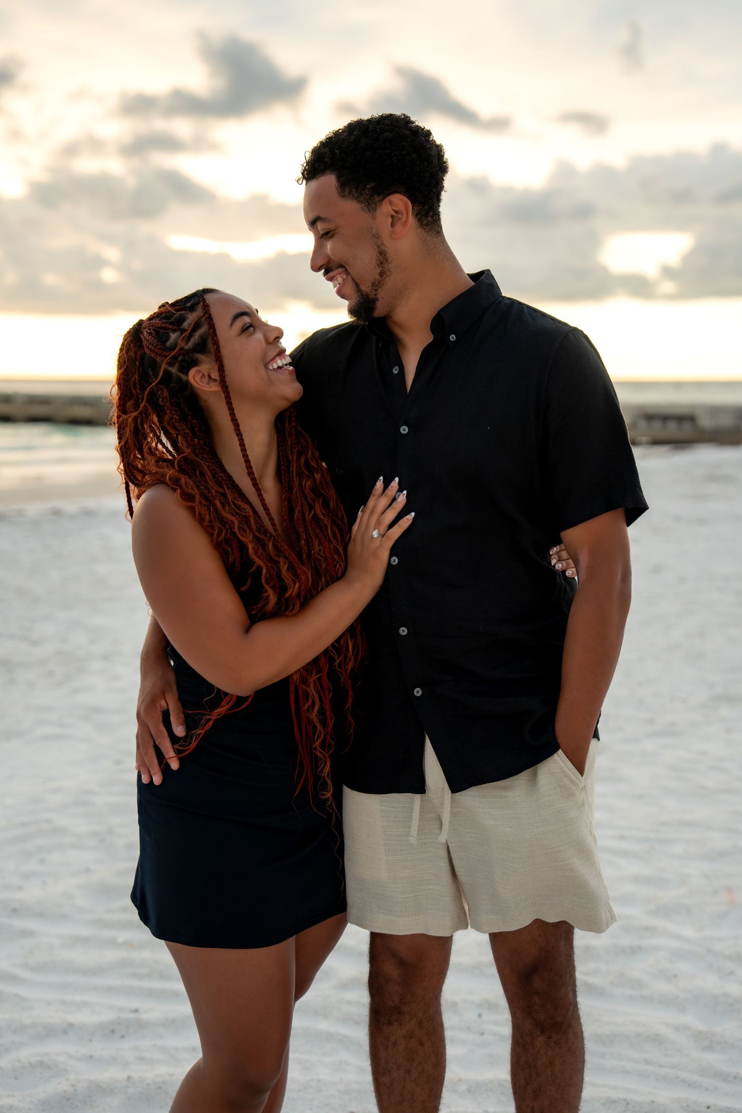 Happy couple in matching black outfits sharing a romantic moment on the beach at sunset.