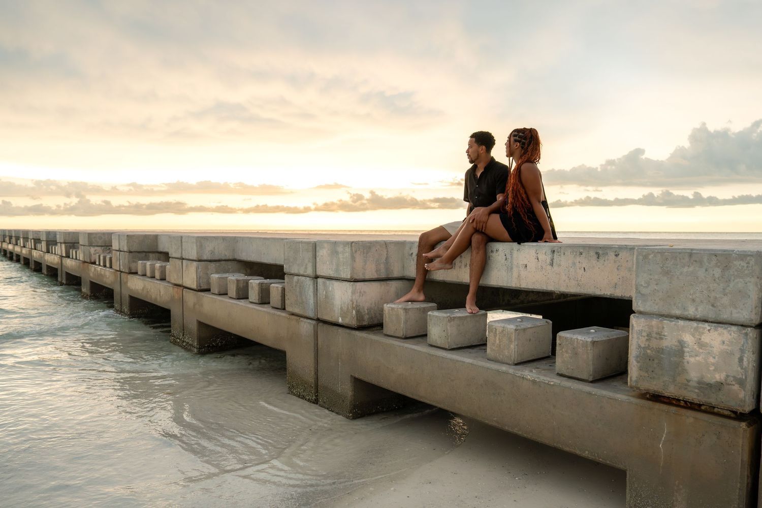 Romantic couple sitting on a concrete pier overlooking the ocean during a beautiful sunset.