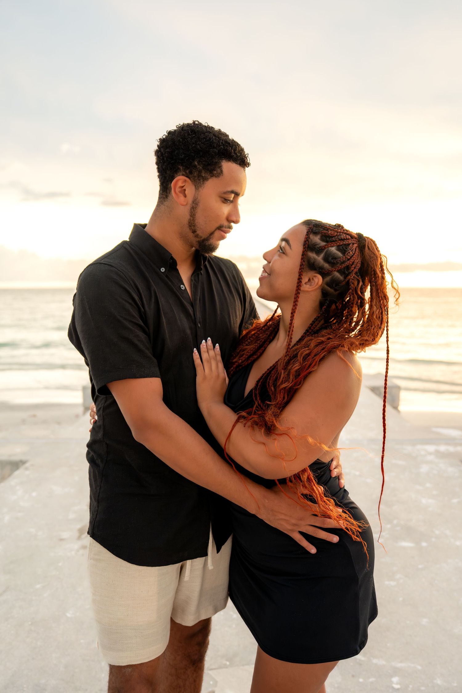 Couple embracing and gazing into each other's eyes on a beach at sunset.
