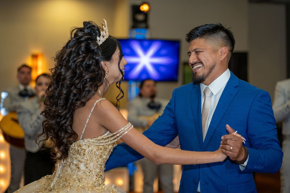 Father and daughter dancing together at an elegant indoor celebration with warm lighting.