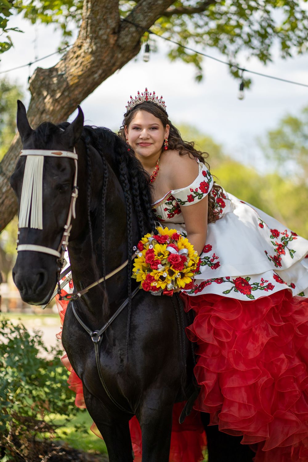 A red and white ballgown is photographed with a black horse adorned with colorful floral decorations.
