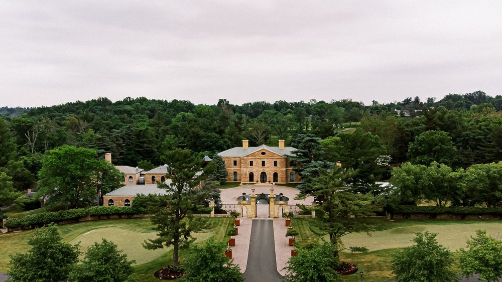 Aerial view of a grand mansion with symmetrical landscaping and a long driveway leading to the estate.