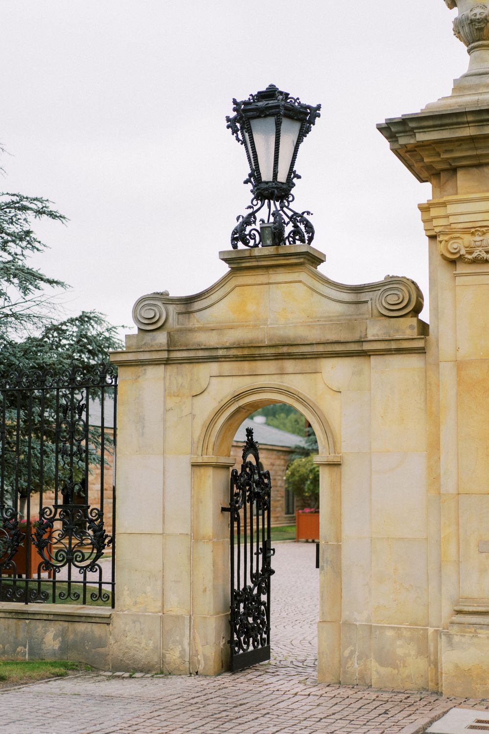 Stone entrance gate with ornate ironwork and classical architectural details at a grand estate.