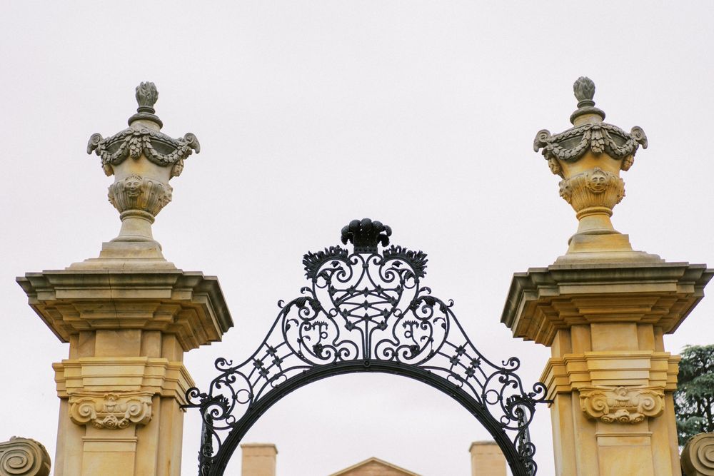 Ornate wrought iron archway with decorative finials atop two stone pillars at an estate entrance.