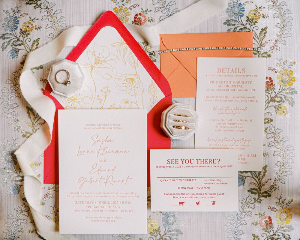 Wedding invitation suite featuring coral red and peach details with floral accents on white paper.