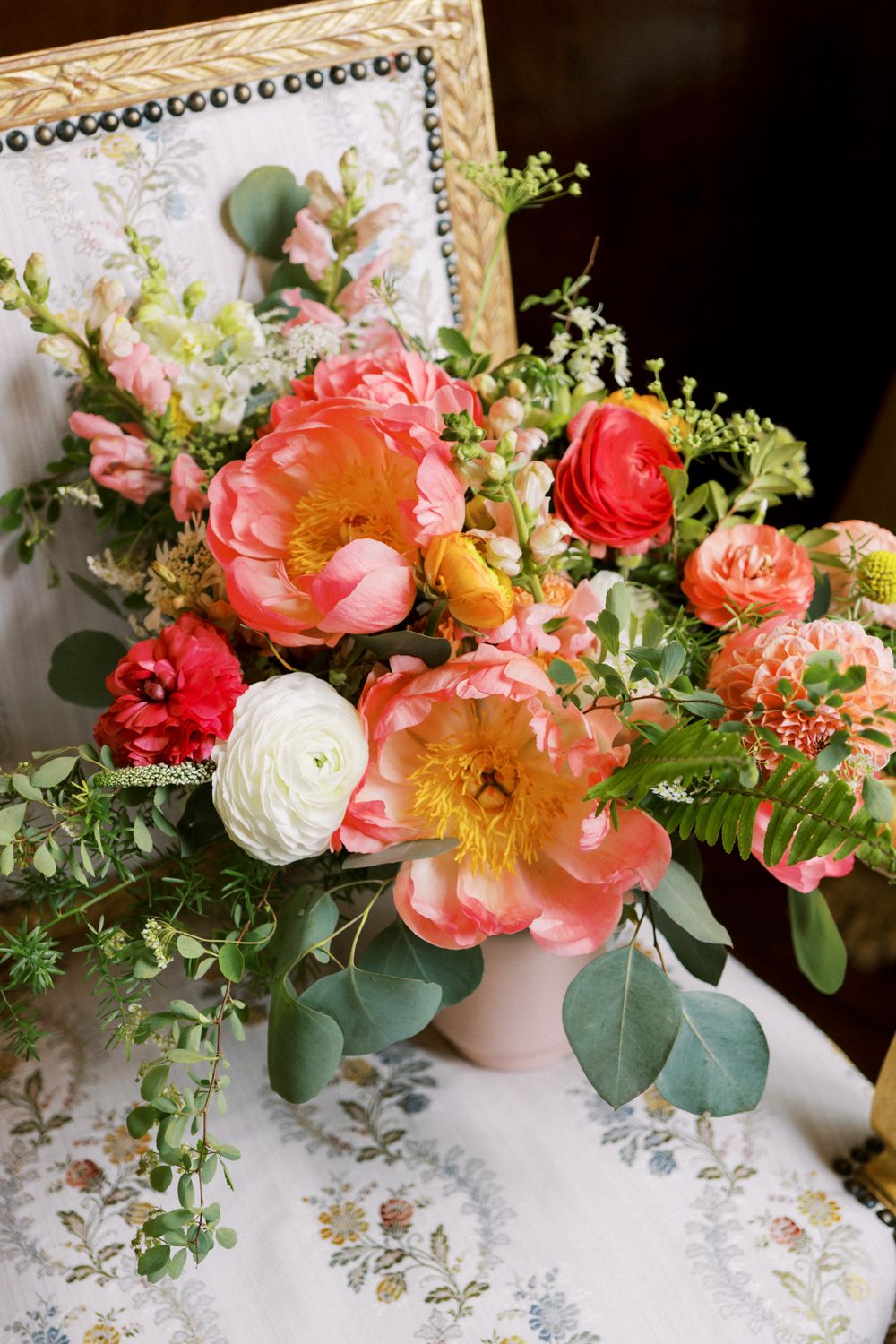 A series of romantic floral arrangements with coral peonies and greenery in soft blush vases on a patterned tablecloth.